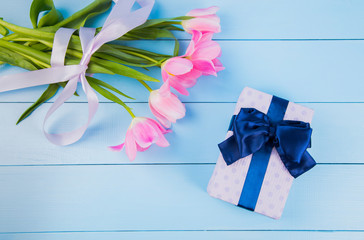 Bouquet of tender pink tulips with gift box on blue wooden background