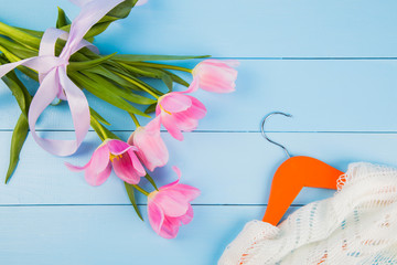 Bouquet of tender pink tulips and hanger with clothes on blue wooden background