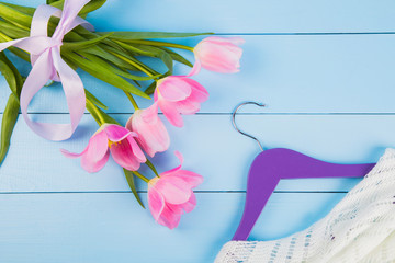Bouquet of tender pink tulips and hanger with clothes on blue wooden background