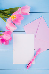 Bouquet of tender pink tulips with empty paper on blue wooden background