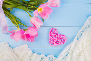 Bouquet of tender pink tulips with heart and fabric on blue wooden background