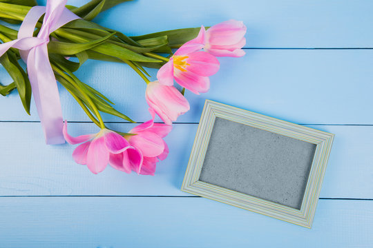 Bouquet of tender pink tulips with empty photo frame on blue wooden background