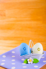 Colorful Easter eggs in basket with flower on fabric on wooden background