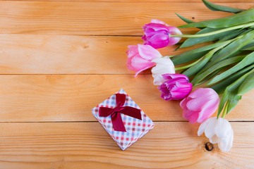 Bouquet of tender pink tulips with gift box on light wooden background
