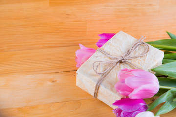 Bouquet of tender pink tulips with gift box on light wooden background