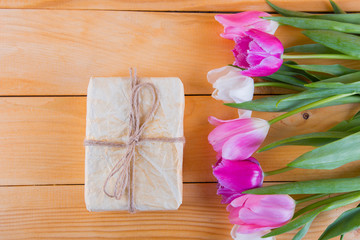 Bouquet of tender pink tulips with gift box on light wooden background