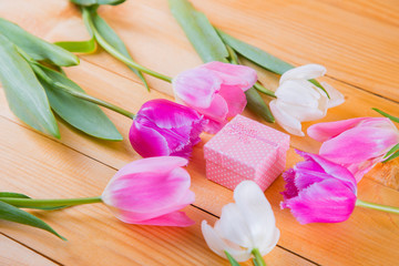 Bouquet of tender pink tulips with gift box on light wooden background