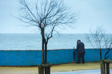 An elderly man suffering from prostate adenoma - prostatit, relieve themselves while walking in the rain on the waterfront. The concept of the medical theme. Illustration diseasesymptoms.