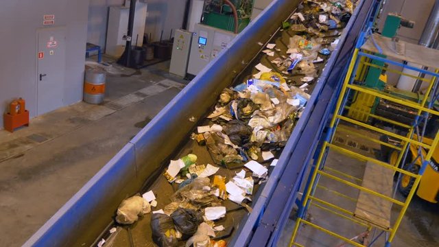Trash, rubbish, litter on a working sorting conveyor belt in a recycling plant. 4K.