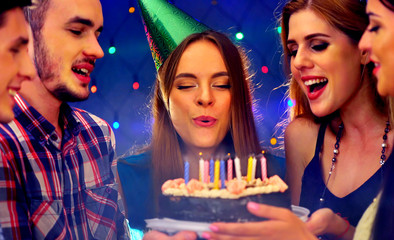 Happy friends birthday party with candle celebration cakes. People looking at burning candles. Two women and men have fun in nightclub.