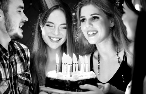 Black white pictures of happy friends birthday wear in hat party with candle celebration cakes. People looking at burning candles. Two women and man have fun.