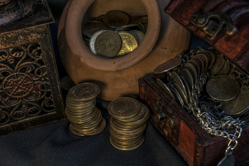 Fototapeta na wymiar Treasure chest, pile and pillar of coins, a ceramic bowl filled with jewelry coins and candle lamp in dark environment 