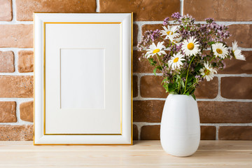 Gold decorated frame mockup with wildflowers bouquet exposed brick wall