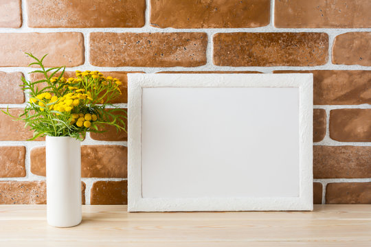 White landscape frame mockup with yellow flowers near exposed brick walls