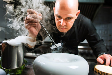 Chef is concentrated on preparing modern molecular dish with pincers and liquid nitrogen