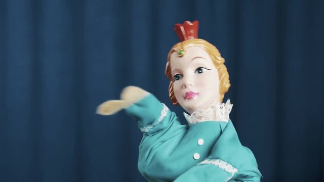 Princess in blue dress and red crown hand puppet toy appears on scene and do hip hop movements, shaking head with blue crease curtains background