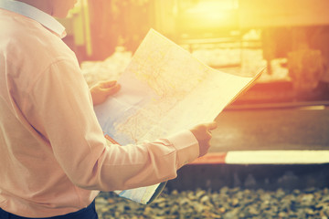 Obraz premium travelling concept.Relax time of businessman traveler holding location map and looking for some direction,business man holding map, waiting for a train at train station,selective focus,vintage color.