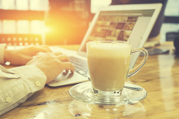 cup of coffee and businessman working on a laptop at office desk with paperwork and other objects on old wooden table in background, Selective focus,Vintage tone