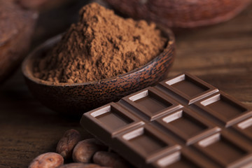 Chocolate bar, candy sweet, cacao beans and powder on wooden background