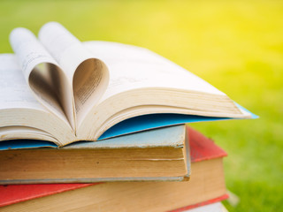stack of books on table in garden with top one opened and pages forming heart shape