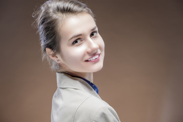 Portrait of Young Sensual Caucasian Girl in Jacket Looking backwards and Smiling. Against Brown...