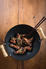 Chicken wings in a black wok, overhead shot. Wooden tabletop. Copy space