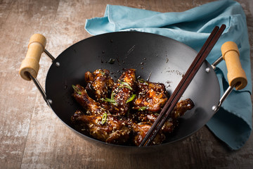 Chicken wings in a wok, sticky sauce, Wooden background. 