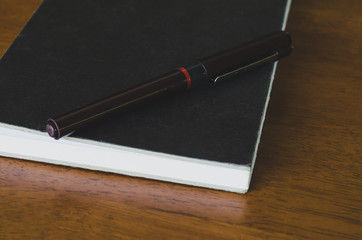 pen and notebook on wood table . vintage style tone .