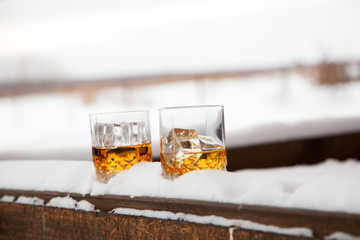 Two whiskey glasses in the snow on a winter background.