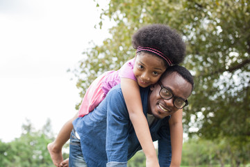 Fototapeta premium African American father and daughter playing and carrying on back in green park scene