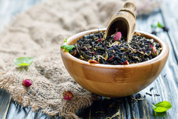 Dry black tea with flower petals in a wooden bowl.