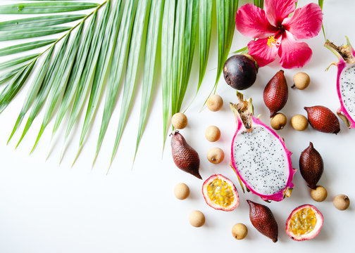 Tropical background of palm leaves and fruit on a white. Passion fruit, longan, mangosteen, pitahaya, mangon, salakh flat top view.