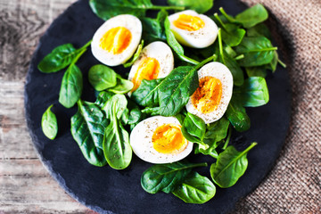  Boiled eggs cut in a half  with Fresh green spinach baby leaves on wooden background with copy space