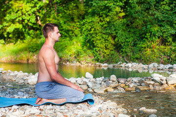 Man meditating near the mountain river. Yoga practicing outdoors.