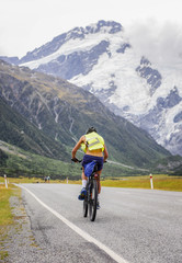 man riding bicycle touring on the road of mountain in background, in new zealand