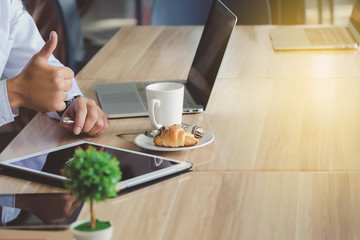 Businessman using hands and fingers tablet to work and Now thumbs. The notebook, cup of coffee, toast, a blurred background. In the morning light.