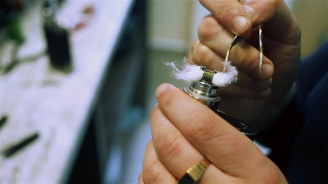 Male hands fill cotton wool in to an e-cigarette for vaping. After-sales service of the electronic cigarette. ENDS.