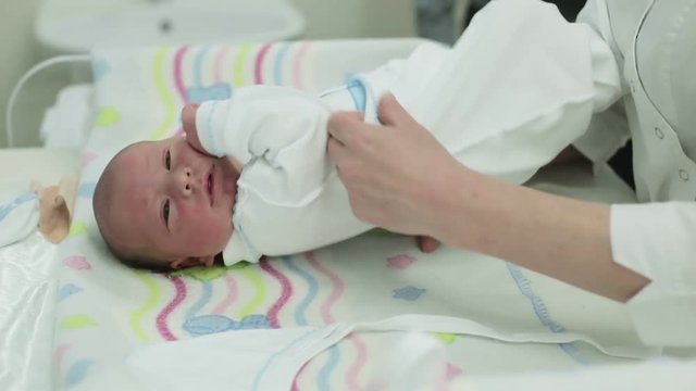 Nurse swaddle newborn baby after birth on table.