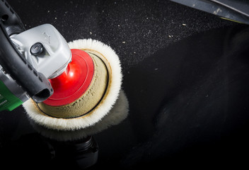 The man is polishing the black car with polish machine.