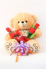 Brown teddy bear with a red rose and a gift box on a white background.