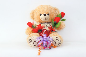 Brown teddy bear with a red rose and a gift box on a white background.