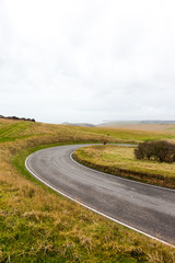 Fototapeta premium Empty streamers wave lack road in green fields with cloudy sky over horizon