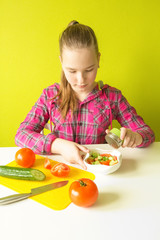 A young girl prepares a salad of fresh vegetables tomato and cucumber