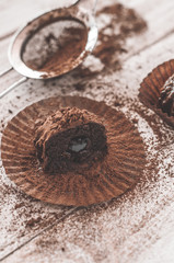 Chocolate chip muffin in brown wax paper. Unwrapped. Cocoa powder in the background