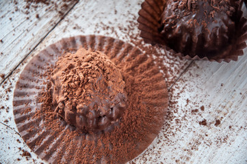 Chocolate chip muffin in brown wax paper. Unwrapped. Cocoa powder in the background