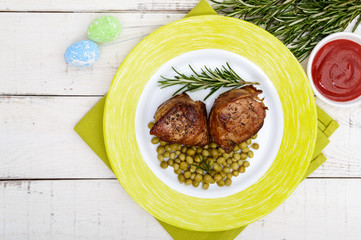 Juicy pork medallions wrapped in bacon, serve with green peas and a sprig of rosemary on a plate. The top view.