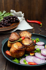 Juicy pork medallions wrapped in bacon, serve on the iron pan on the dark wooden dackground.