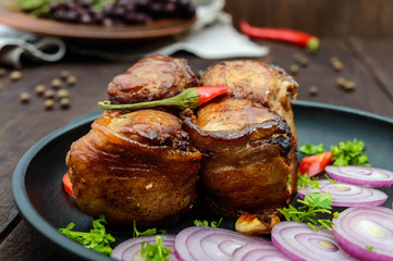 Juicy pork medallions wrapped in bacon, serve on the iron pan on the dark wooden dackground. Close up