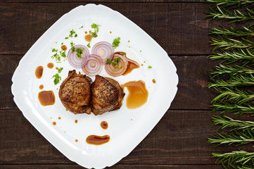 Juicy pork medallions wrapped in bacon on a plate on the dark wooden background. The top view.