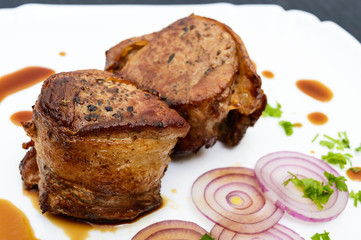 Juicy pork medallions wrapped in bacon on a plate on the dark wooden background. Close up